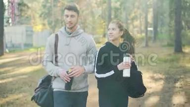 年轻夫妇<strong>正在</strong>公园<strong>里</strong>散步，谈论着拿着运动袋和水瓶，小伙子<strong>正在</strong>喝酒